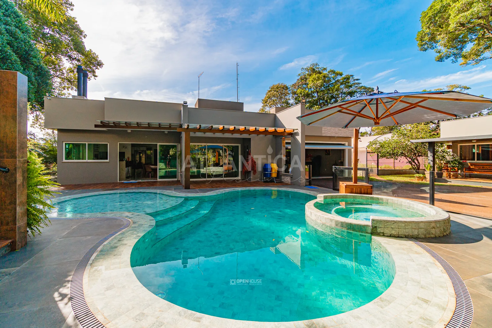 Piscina residencial de linhas curvas com spa circular elevado e residência de linhas horizontais ao fundo