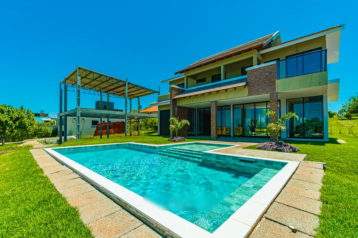 Piscina retangular com hidromassagem integrada em frente à residência, com piso de pedra e gramado