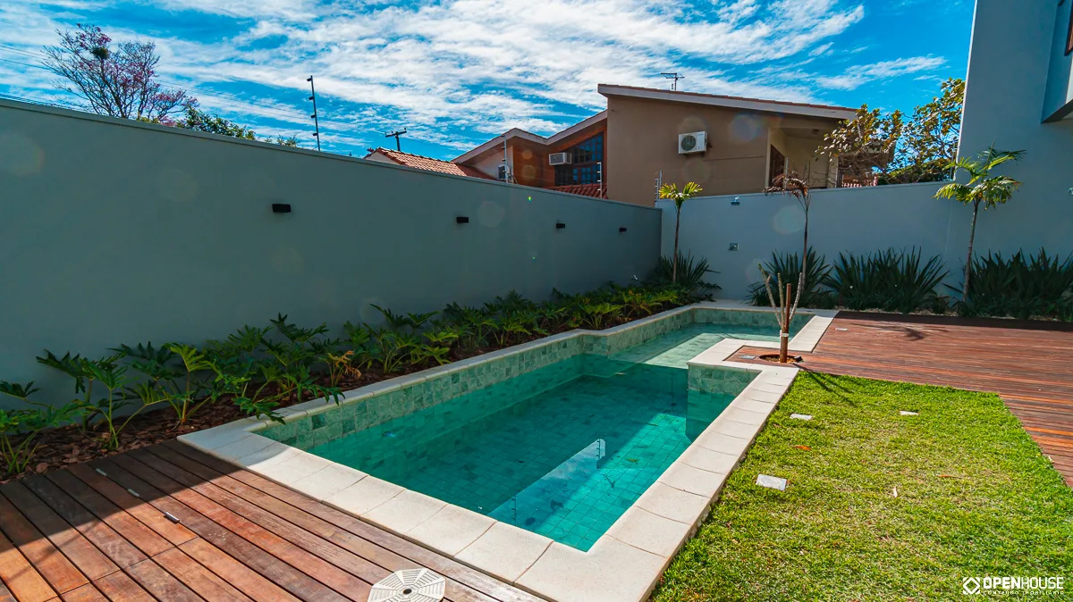 Vista ampla do pátio com a piscina linear, o deck em madeira e a faixa de gramado ao lado