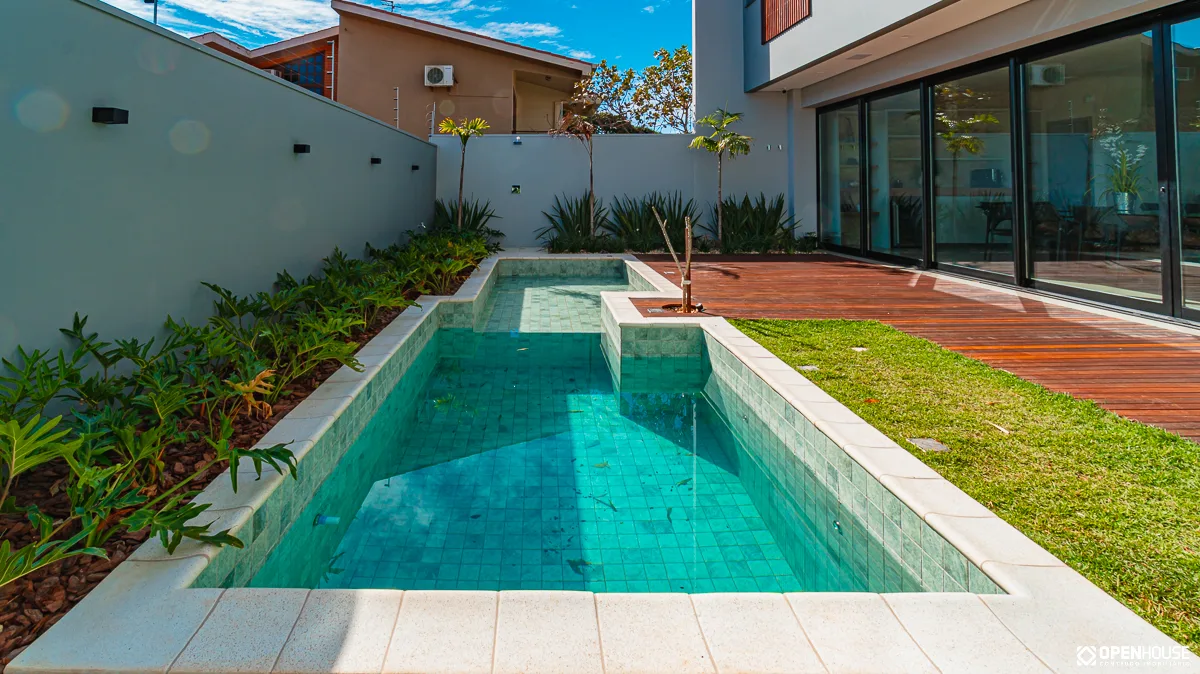 Lateral da piscina junto aos canteiros lineares de folhagens e ao muro do terreno