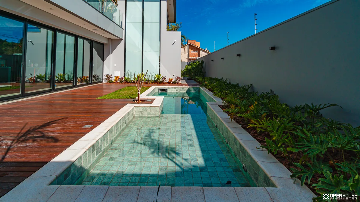 Vista do deck em madeira que acompanha a borda da piscina até a fachada da casa