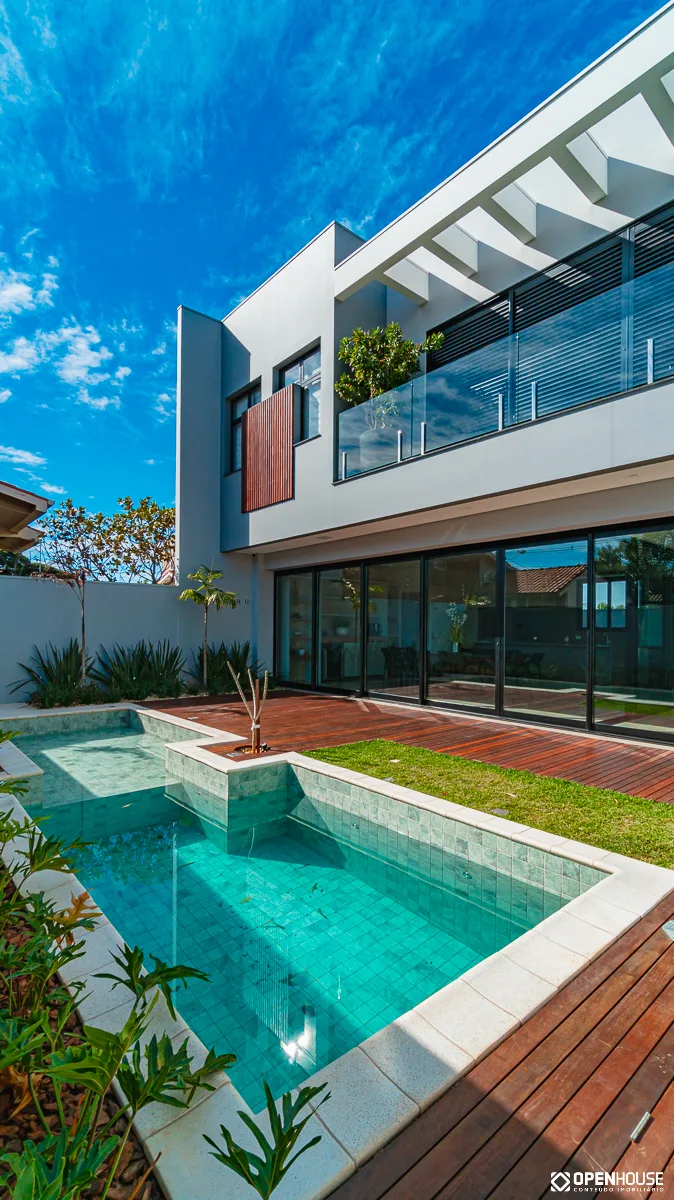 Enquadramento vertical mostrando a piscina, o deck em madeira e a varanda superior da casa