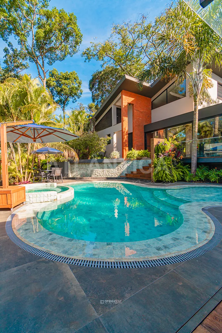 Linhas curvas da piscina com a área rasa em primeiro plano e a fachada da residência ao fundo