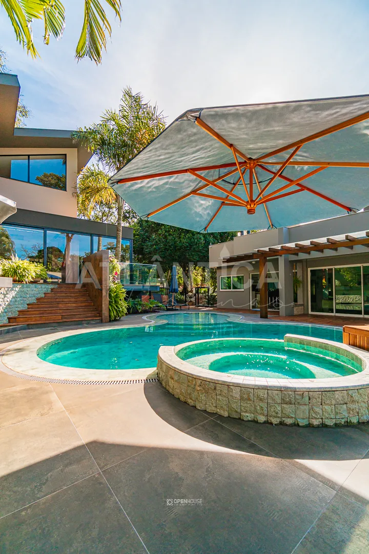 Spa circular elevado revestido em pedra sob guarda-sol amplo, ao lado da lâmina da piscina