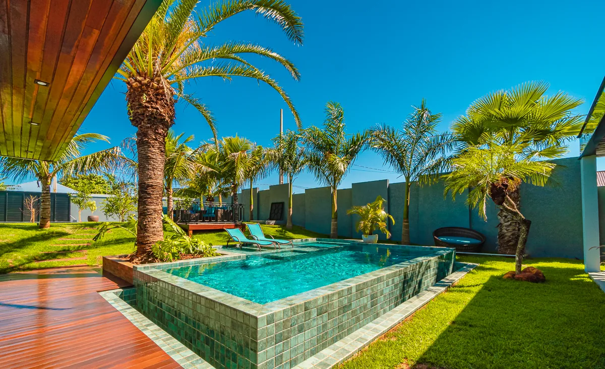 Volume elevado da piscina com face em pastilhas verdes junto ao deck de madeira