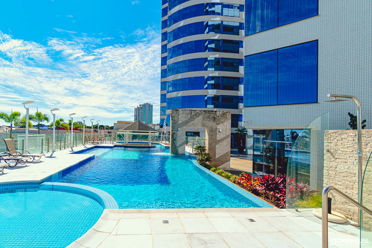 Vista ampla da piscina coletiva de linhas retas com as torres residenciais ao fundo