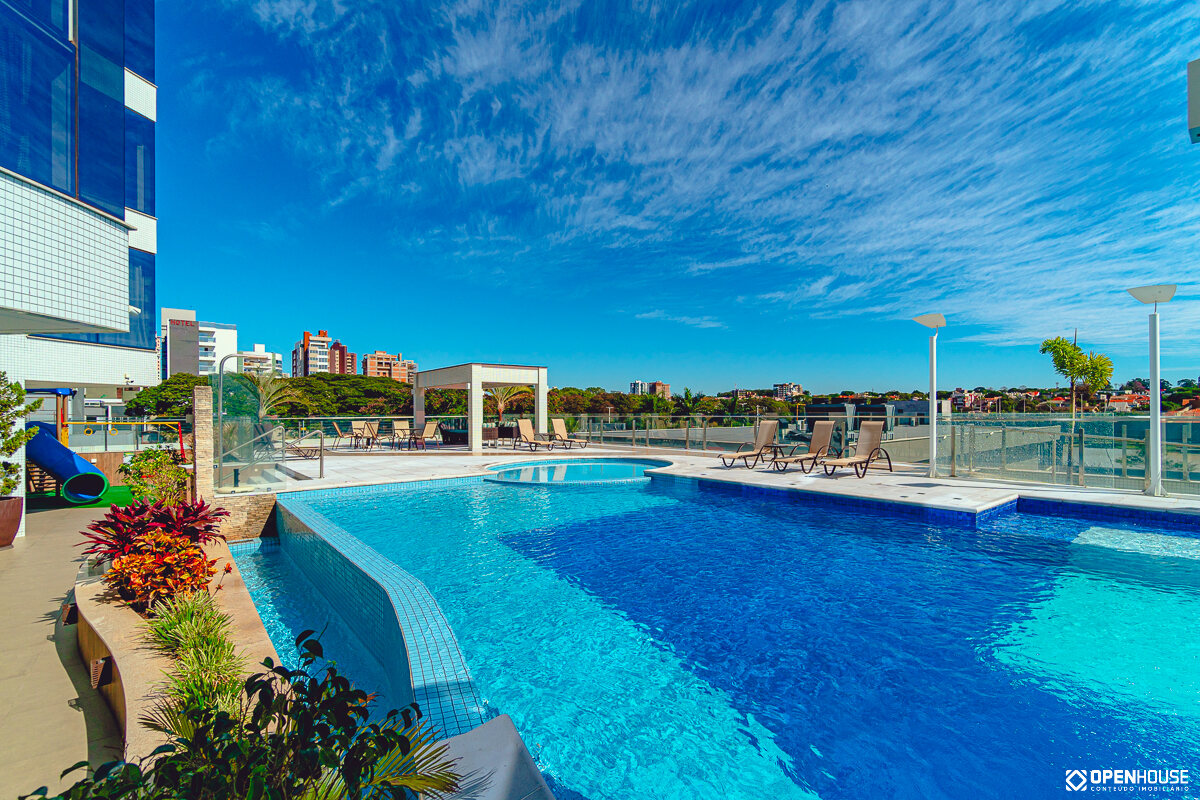 Piscina coletiva com canteiros de paisagismo na borda e vista aberta para a cidade