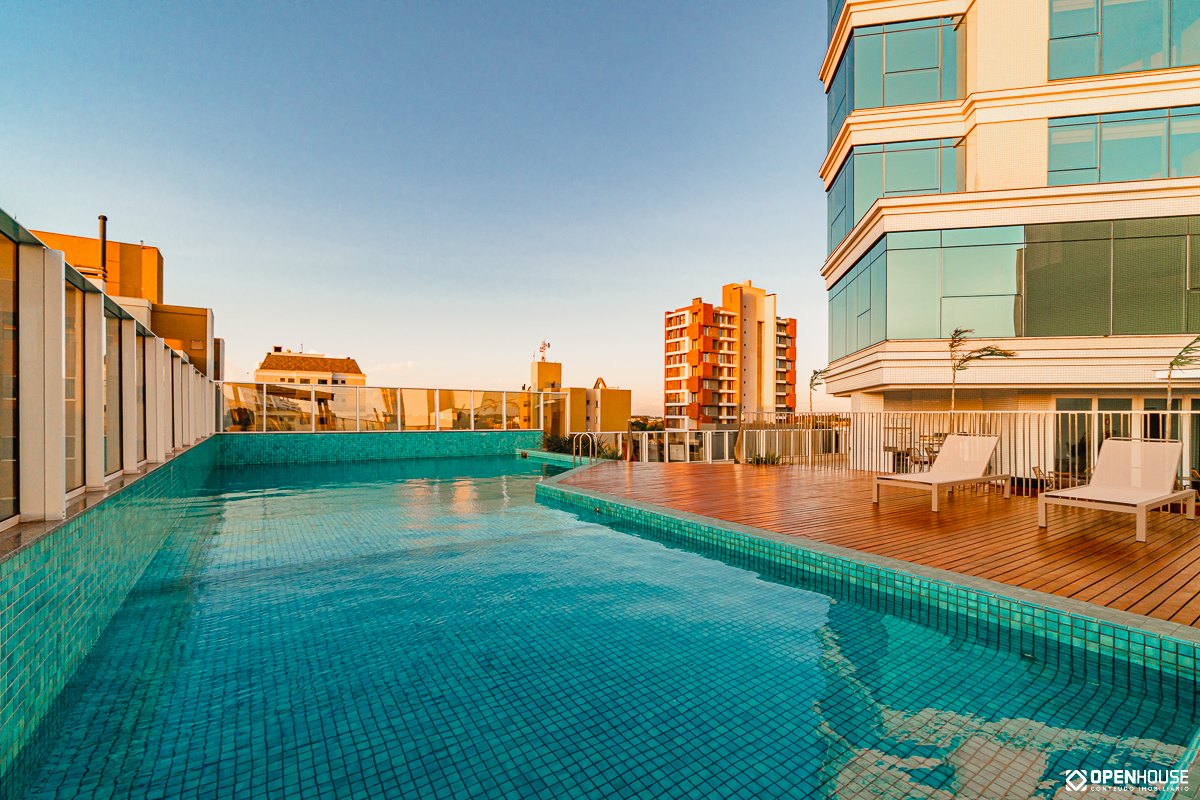 Piscina coletiva em pavimento elevado do edifício, com deck de madeira e vista para a cidade