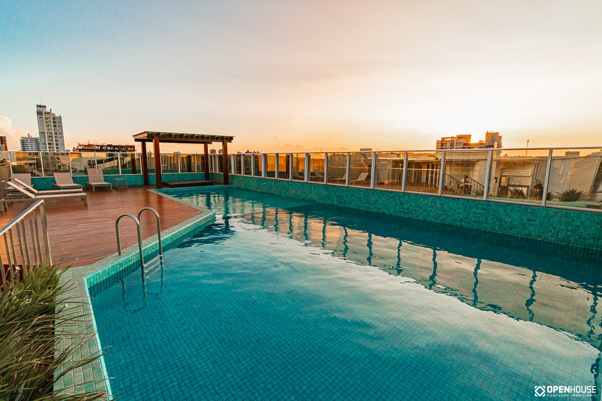 Lâmina de água e deck de madeira sob a luz de fim de tarde, com guarda-corpo de vidro ao fundo
