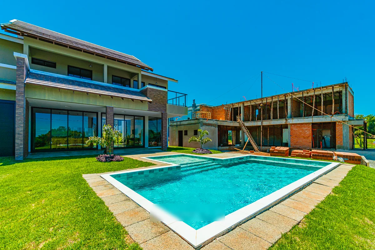 Piscina vista da lateral, com a varanda coberta e o pano de vidro da residência ao fundo
