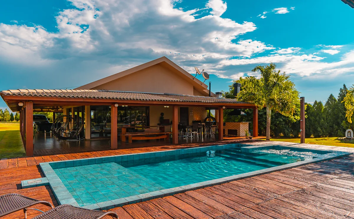 Piscina vista em contraluz, com o sol acima e o deck em réguas de madeira em primeiro plano