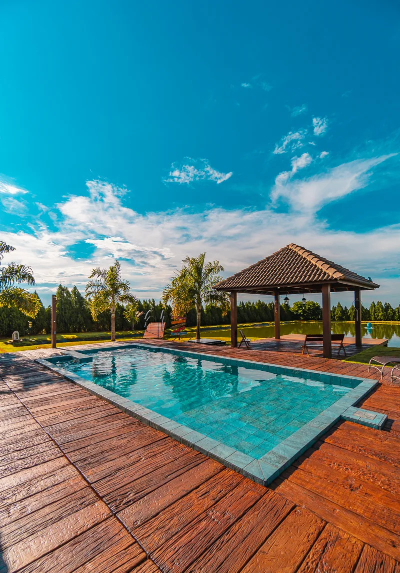Piscina em primeiro plano com gazebo ao fundo e o lago da fazenda no horizonte