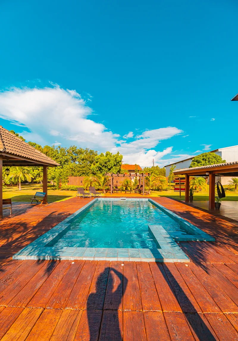 Piscina alongada com o entardecer refletido na água e a varanda coberta ao lado